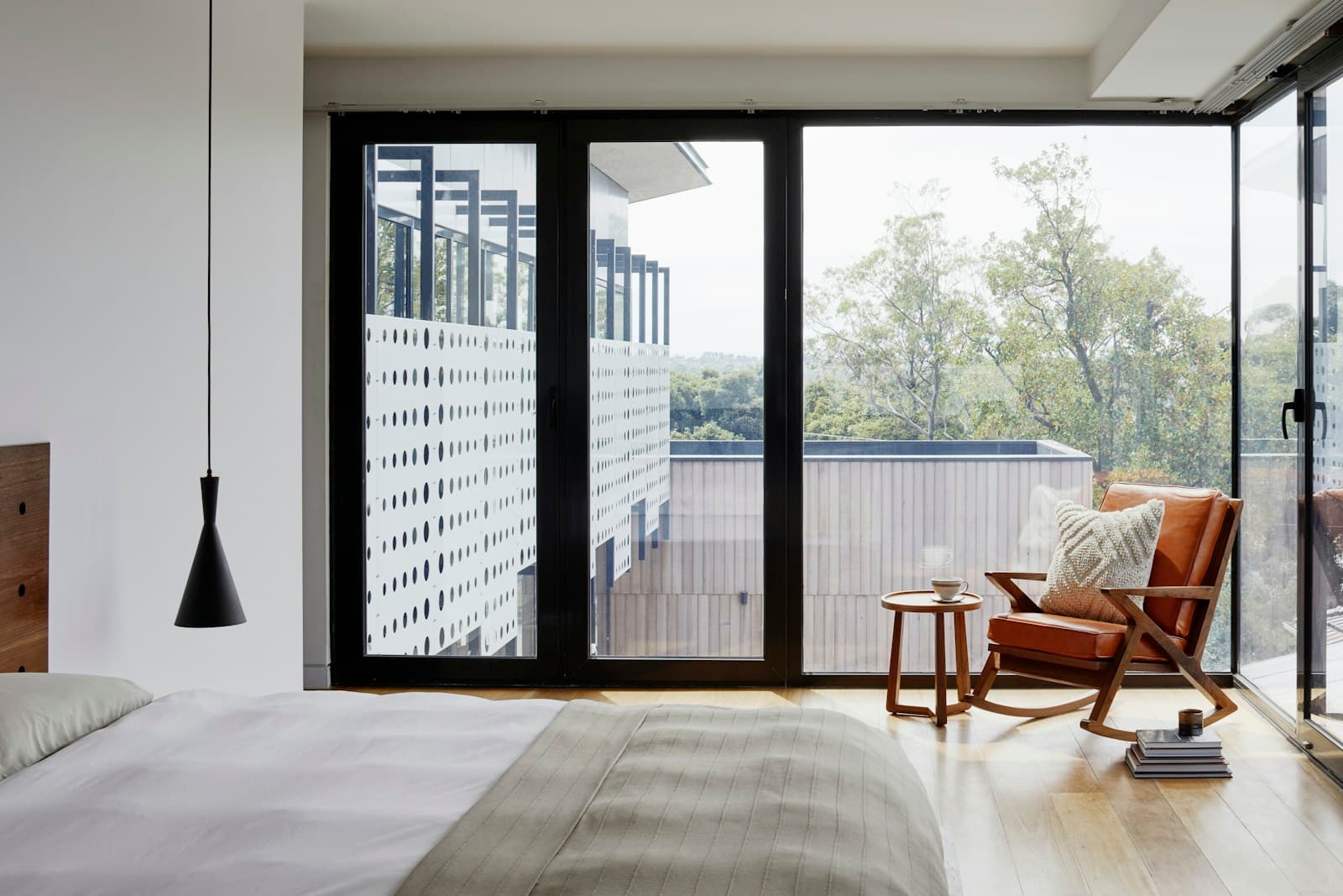 Real master bedroom with floor-to-ceiling glass, natural wood floor, and armchair